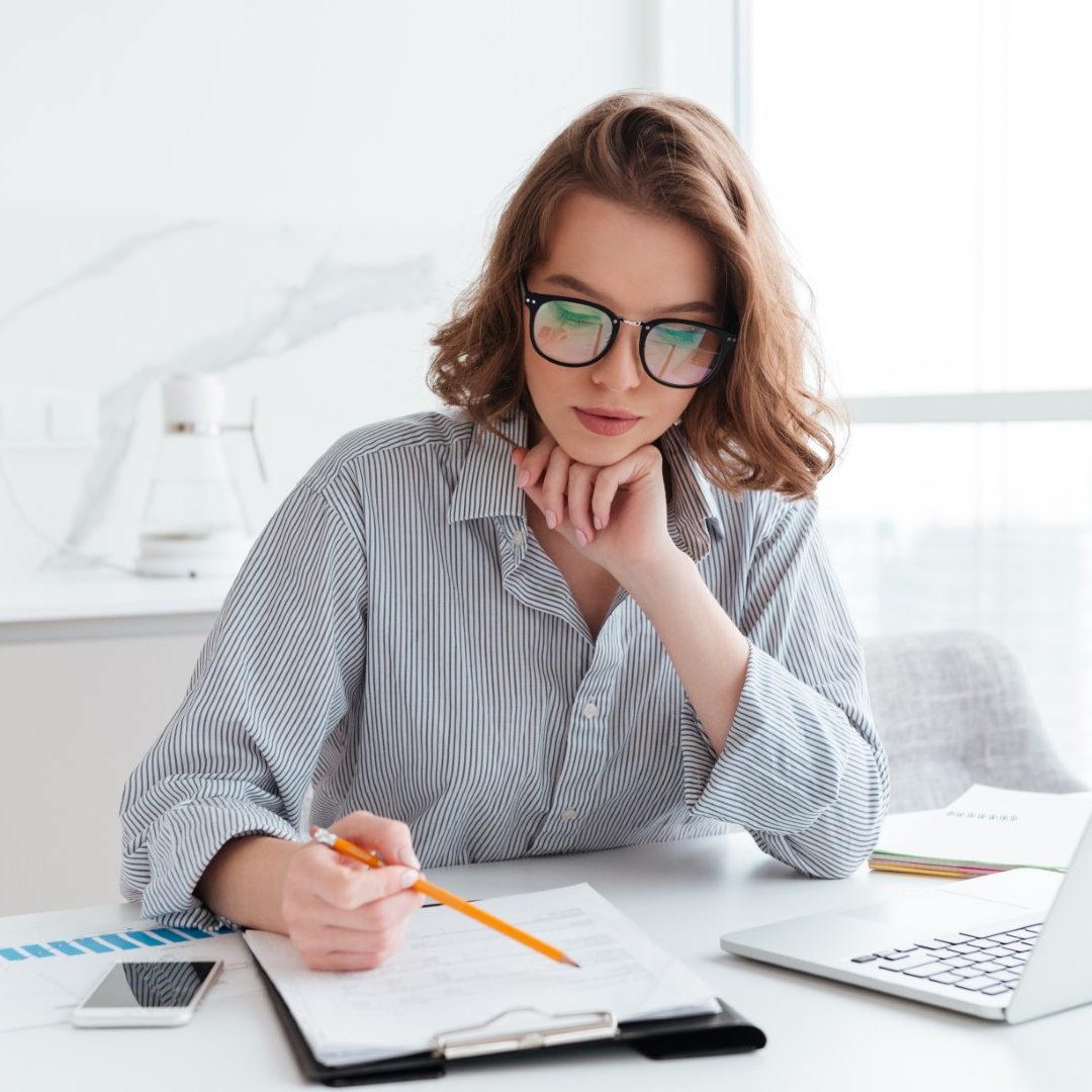 Young concentrated businesswoman in glasses and striped shirt working with papers at home